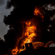 A firefighter works to extinguish an oil well set on fire as plumes of smoke rise against a dark sky.